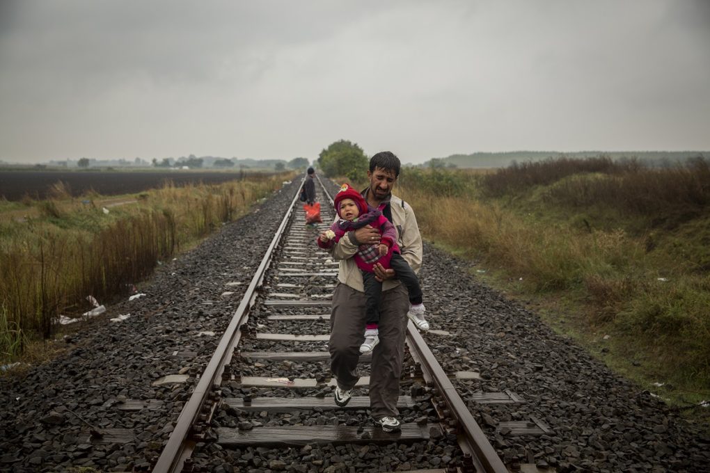 Un padre camina por las vias del tren llevando a su hijo en brazos unos cientos de metros despues de haber cruzado la frontera entre Serbia y Hungria entrando en la localidad de Roszke. Roszke. Hungria.  Olmo Calvo. (10/09/2015)